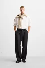 Pantalón negro de corte ancho con cinturón de tela con hebilla metálica y pliegues frontales.