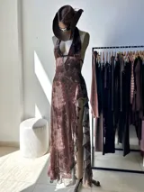 Vestido largo de mujer, color marrón con estampado tipo tie-dye o marmolado en tonos rosados y grises. Diseño halter con escote profundo en V y tiras finas en la espalda. Presenta un corte cruzado en el busto y una abertura lateral con volados en cascada.