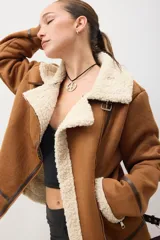 Campera marrón de gamuza sintética con interior de piel sintética color crema. Tiene cierre cruzado con cremallera y hebilla en el cuello.