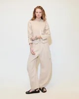 Pantalón de lino color beige, de tiro medio, con pinzas, silueta comba en piernas y largo hasta los tobillos.