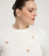 Remera blanca de algodón con cuello redondo y mangas cortas. Presenta pequeños corazones bordados con lentejuelas en el frente.
