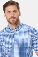 Camisa de manga corta con estampado a cuadros azules y blancos, bolsillo en el pecho con logo bordado y botones personalizados. Hecha en Uruguay.