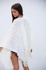 Poncho blanco de tejido calado con diseño geométrico y flecos en el borde.
