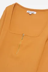 Remera de manga larga color mostaza, confeccionada en tejido acanalado, con escote cuadrado y cierre frontal metálico dorado.