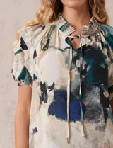 Blusa estampada con cuello fruncido y lazo, mangas cortas con volados.