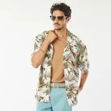 Camisa de manga corta blanca con estampado de hojas en tonos marrones, verdes y amarillos. Tiene cuello clásico, cierre frontal con botones y corte recto.