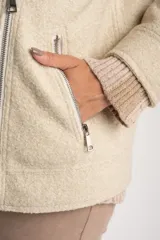 Campera de abrigo color crema, con cuello solapa y cierre frontal asimétrico. Presenta textura bouclé o de lana rizada.