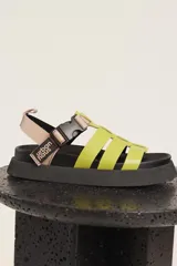 Sandalias Urban Haus con tiras anchas cruzadas color verde lima, ajuste con hebilla y plataforma plana color negro.