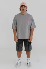 Remera gris de corte holgado con estampa en la espalda con la frase 'Mentally Gone' en rosa y un rostro abstracto en blanco.