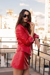 Conjunto de chaqueta y falda de cuero sintético color rojo. La chaqueta es corta, con cierre frontal y solapas. La falda es corta, de corte recto y tiro alto.