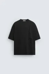 Camiseta negra de corte holgado, cuello redondo y manga corta. Estampado vertical con texto y diseño abstracto en el frente.
