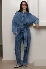 Mameluco de jean celeste con efecto nevado vintage, corte holgado, cuello mao, cierre frontal con botones y cinturón de lazo.