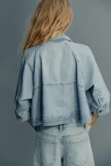 Cazadora de denim celeste con cuello solapa y manga tres cuartos. Cierre frontal con botones metálicos.