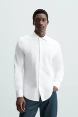 Camisa celeste a rayas verticales blancas, de corte recto, con cuello italiano abierto, mangas largas con puños abotonados y cierre frontal con botones.