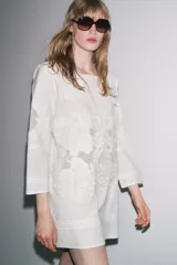 Vestido corto de algodón y lino color blanco, con cuello babero cuadrado, manga larga y bordados florales. Cierre en la espalda con abertura y botón.