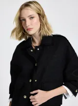 Chaqueta corta negra de tela tejida con cuello alto, mangas largas con puños abotonados, dos bolsillos delanteros con solapa y cierre frontal con botones.