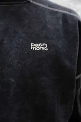 Buzo negro de frisa 100% algodón con calce oversize y lavado gastado. Presenta costuras a contratono, recortes y logos estampados en el frente y en el puño.