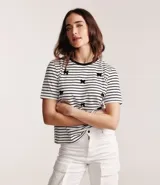 Blusa de media malla a rayas horizontales blancas y negras, con cuello redondo y mangas cortas. Aplicación de moñas negras.