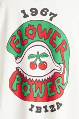 Remera blanca de corte amplio con cuello redondo y mangas cortas. Estampado pequeño con la palabra "PACHA" en rojo en el lado izquierdo del pecho.