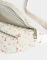 Riñonera color crema con estampado de flores pequeñas, correa ajustable con hebilla metálica, cierre superior y bolsillo frontal con cierre.