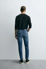 Pantalón de jean azul oscuro con efecto lavado y roturas en las rodillas, de corte ajustado al cuerpo desde la cintura hasta el tobillo.