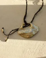 Collar con dije circular dorado con abertura central, realizado en bronce macizo y colgante de hilo de seda natural negro con detalles de cuentas doradas en los extremos.