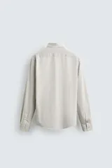 Camisa de manga larga con cuello italiano y cierre frontal de botonadura. Presenta un patrón de rayas verticales finas en tonos blanco y verde claro.