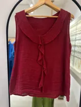 Musculosa color bordó de tejido ligero, posiblemente lino o una mezcla, con cuello en V amplio y un volante o cascada de tela fruncida que cae verticalmente por el centro del frente.