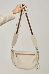 Bandolera de cuero celeste con correa de cinta regulable, forro de algodón, cierre central y bolsillo trasero con cierre.