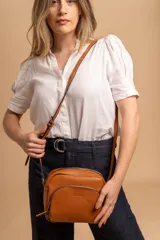 Bandolera de cuero sintético color beige, con diseño compacto y elegante. Cuenta con un bolsillo frontal con cierre y un compartimento principal con cierre. La correa es regulable.