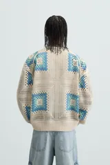 Cárdigan de punto color crudo con diseño de cuadrados de crochet en tonos celeste y azul. Tiene cuello en V, manga larga, bolsillos frontales y cierre con botones.