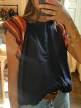 Top negro con mangas cortas tejidas a rayas horizontales en tonos naranja y azul.