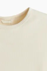 Remera color crema de punto acanalado de algodón, de corte entallado, con cuello redondo ribeteado y mangas cortas.