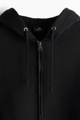 Campera con capucha negra, corte oversized, con cierre frontal, bolsillos y puños acanalados.