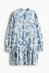 Vestido corto de viscosa con estampado floral en tonos azules. Tiene cuello mao, botones frontales, mangas largas abullonadas con puños abotonados y falda con volantes.