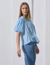 Blusa celeste de gasa marca Zac & Rachel, con cuello redondo, frunces en el frente, mangas 3/4 con puño, abertura central en la espalda y botón.