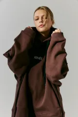 Buzo marrón de frisa con capucha y bolsillos delanteros. Corte oversize, recortes laterales y doble cordón con puntera de goma. Estampa en frente y espalda realizada en serigrafía con diseño de llavero con dijes.