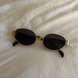 Lentes de sol con marco dorado y lentes ovaladas negras.