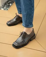 Zapato acordonado de cuero vacuno color marrón oscuro, con suela de goma, horma cuadrada y tacón bajo.