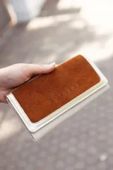 Billetera mediana de cuero color natural con tapa de cuero gamuzado color marrón y logo grabado.