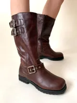 Bota de cuero color marrón con caña media, punta cuadrada, suela track y detalles de hebillas metálicas.