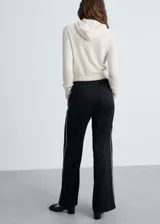 Pantalón de vestir color beige, de corte recto y tiro medio, con cintura elástica y bolsillos laterales. Presenta una raya vertical blanca a lo largo de la pierna.