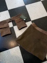 Falda corta de cuero gamuza color marrón oscuro, con diseño utilitario que incluye grandes bolsillos frontales con solapa y un anillo metálico en la cintura. Incluye un cinturón removible a juego.