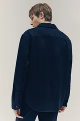 Sobrecamisa azul marino de tejido afieltrado con cuello, botones adelante y canesú en la espalda. Tiene bolsillos superiores con solapa, puños abotonados y bajo redondeado.