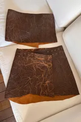 Falda marrón de cuero ovino con textura veteada, corte mini y detalle de ojales metálicos.