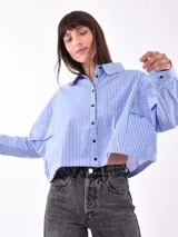 Camisa corta a la cintura, a rayas verticales azules y blancas, con cuello clásico y cierre frontal con botones negros.