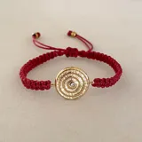 Pulsera tejida roja con dije circular dorado con diseño geométrico y un cristal incrustado.
