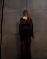 Pantalón largo negro, de tejido transparente con franjas horizontales opacas, corte recto y tiro alto. Se lleva sobre otra prenda.