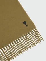 Bufanda de lana color verde oliva, con flecos en los extremos y el logo de corazón 'Ami de Coeur' bordado en negro en un extremo.