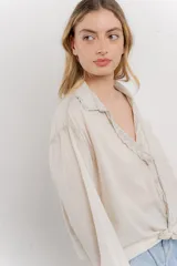 Camisa color crema de manga larga con cuello camisero y detalles de encaje en el escote. Se ata en la parte delantera.